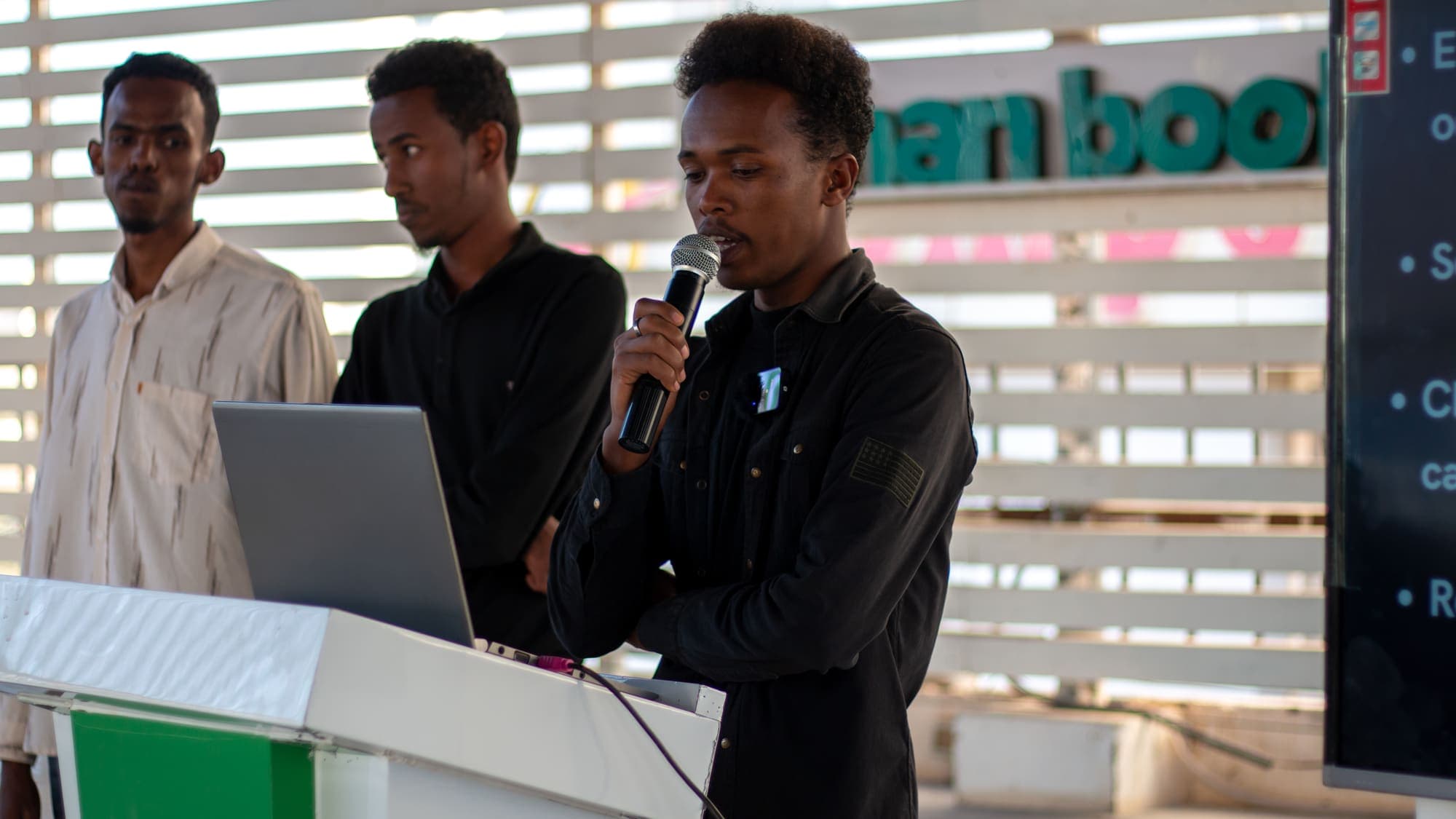 Three young men present together with a microphone and a laptop